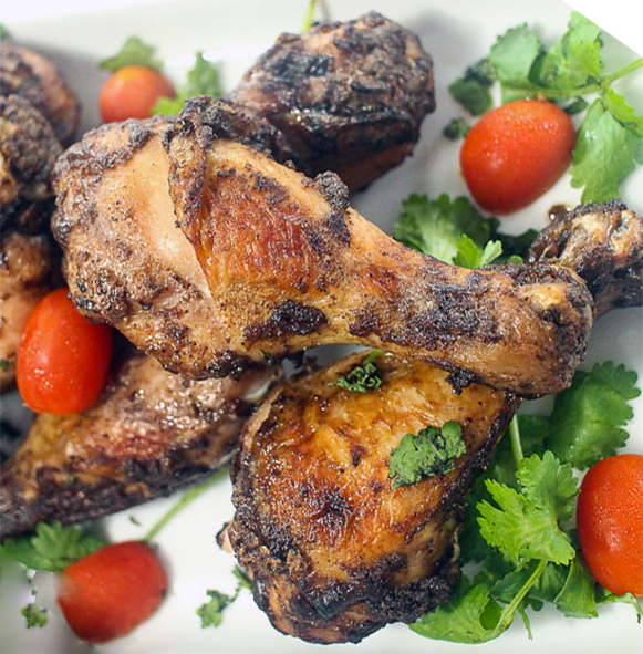 roast chicken drumsticks with advieh spiced coating piled on a plate with baby tomatoes and coriander