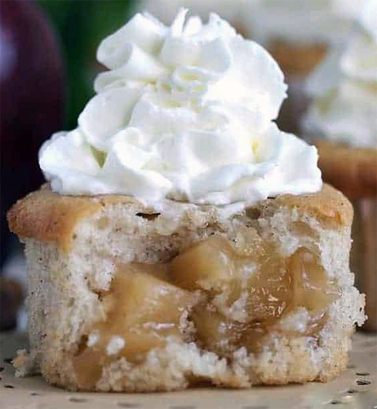 apple cake cupcake topped with whipped cream shown split open to reveal the filling