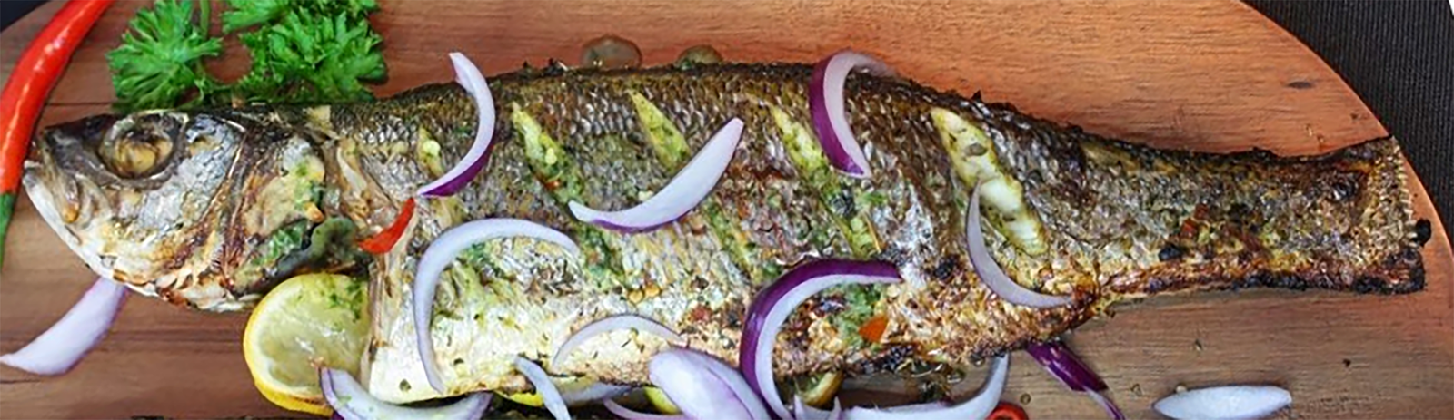 barbecued and oil seared whole sea bass on a wooden board garnished with onions