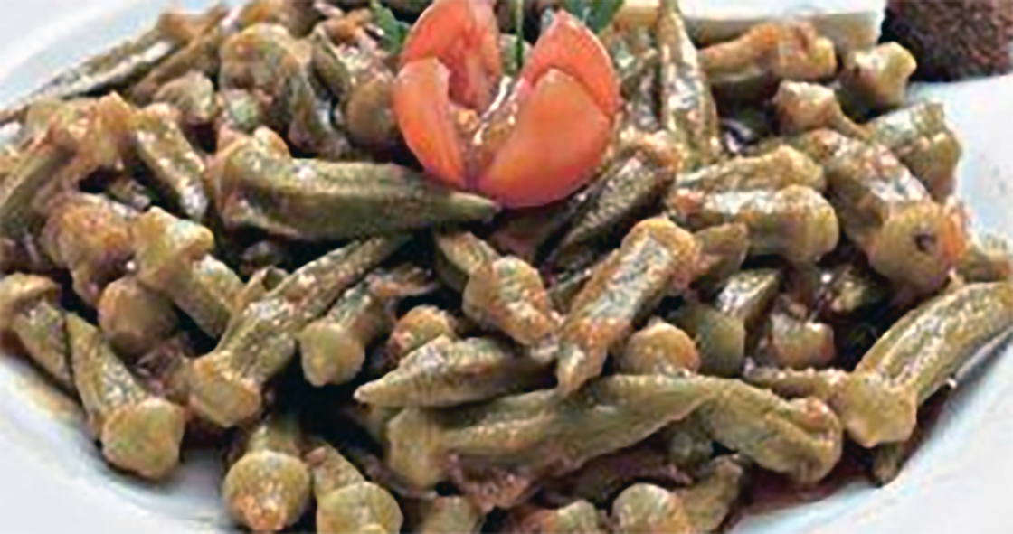 okra cooked in tomato sauce served piled on a plate and topped with a split tomato