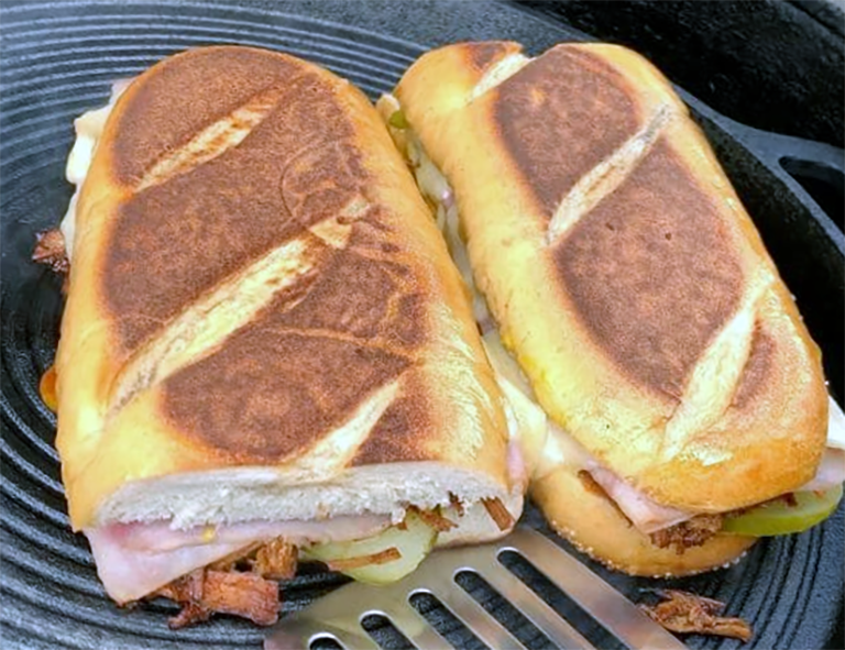 two Cuban sandwich halves heating on a barbecue