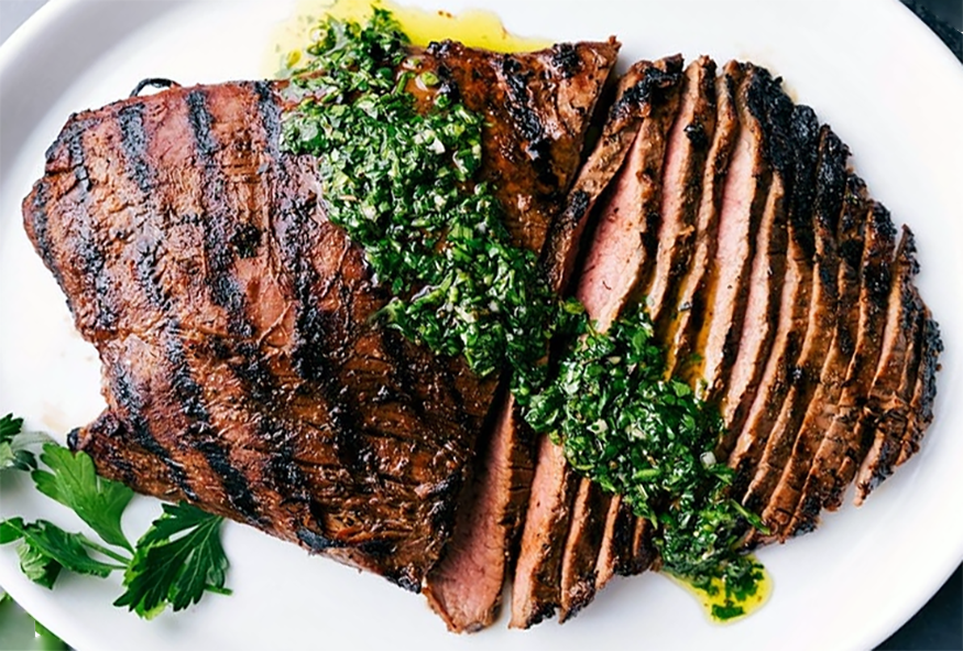 barbecued flank steak served partially sliced and topped with chimichurri sauce