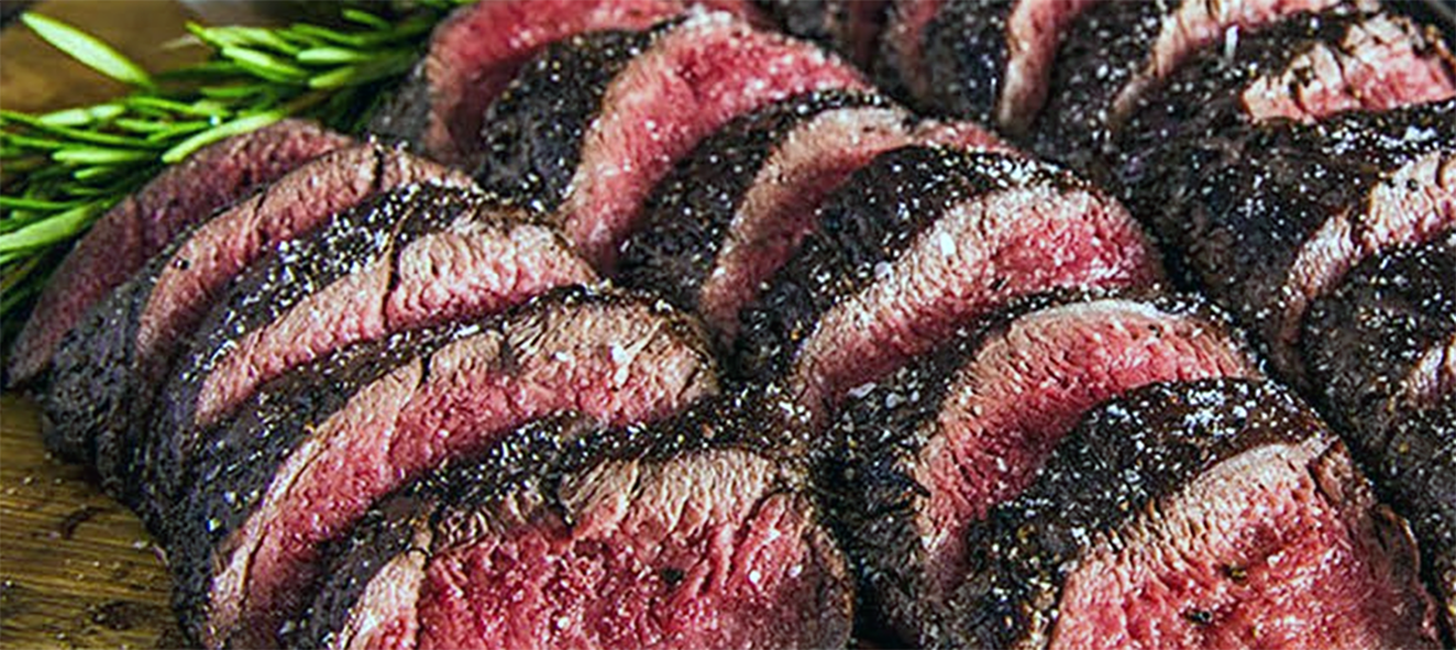 slices of venison fillet barbecued in barbecue sauce served on a wooden chopping board