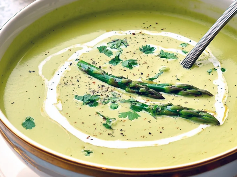 creamy asparagus soup garnished with three asparagus spears and a swirl of cream