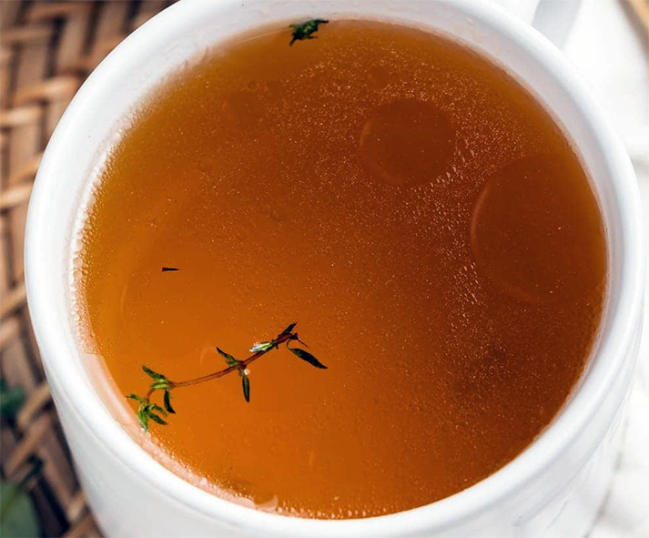 veal consomme in a mug with a sprig of thyme