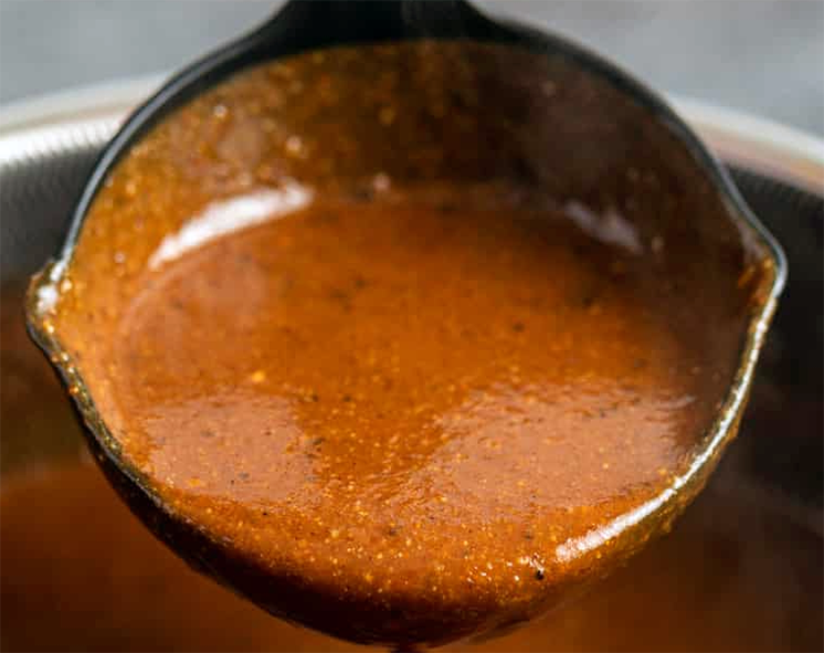 spicy tomato and brown gravy sauce in a ladle