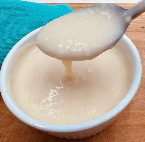 white milk sauce thickened with flour dropping from a spoon into a bowl
