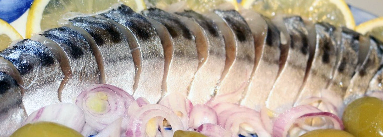 pickled and sliced mackerel arranged on a plate with lemon and red onion