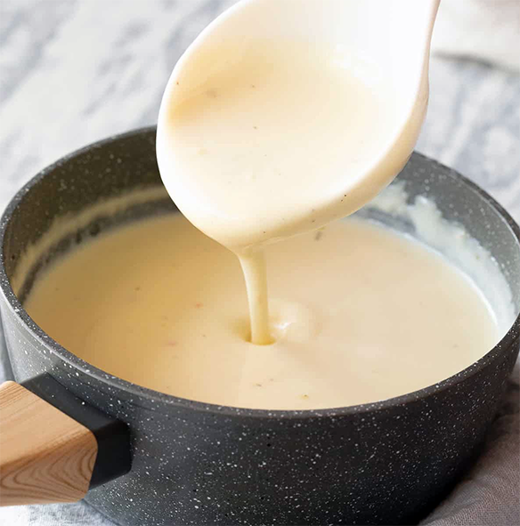 milk and rice flour sauce dropping from a spoon into a saucepan