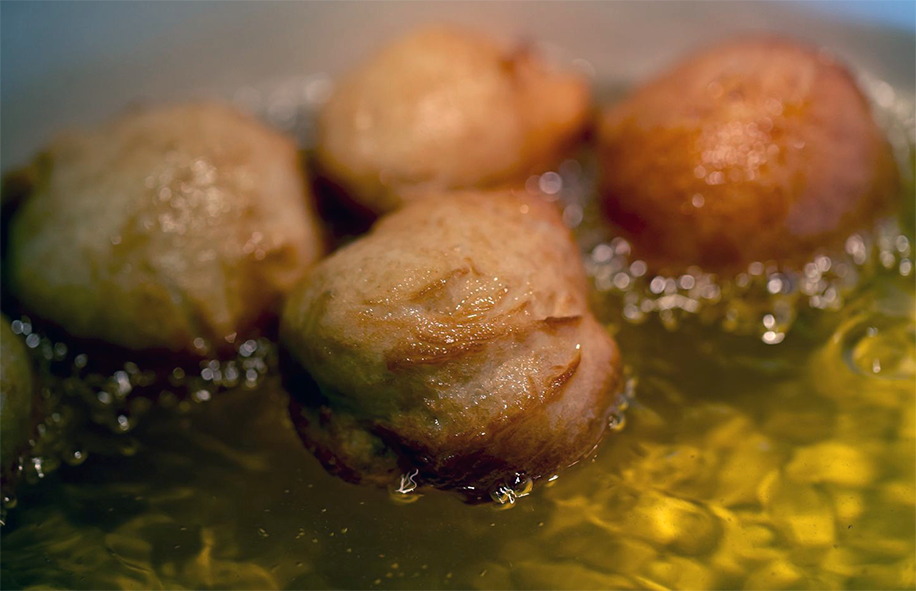 fried dough balls in a meat stock base simmering in a large pot