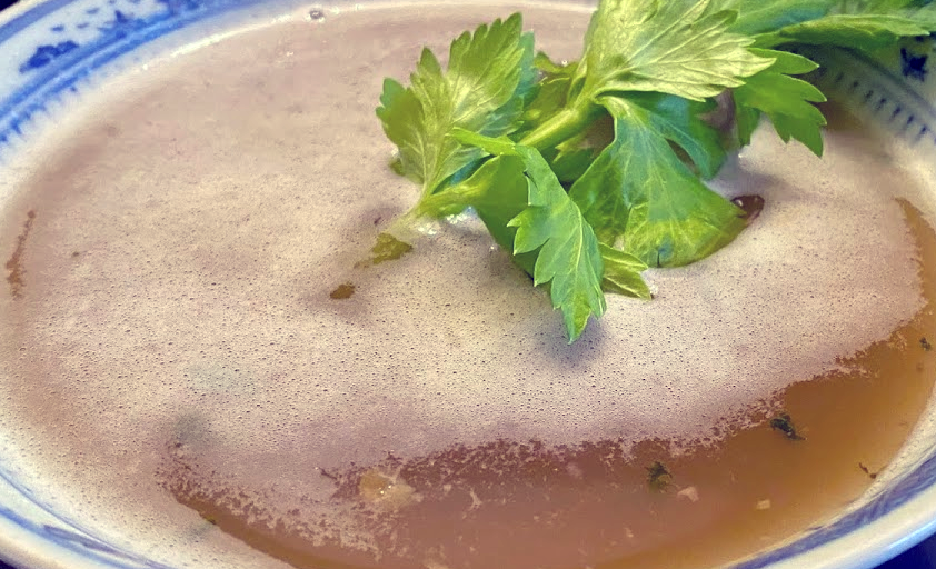 soup maigre served in a bowl with a sprig of celery leaf