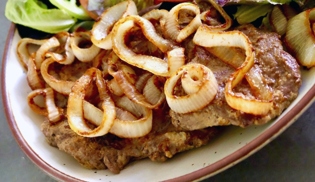 fried steak topped with onions served on a plate
