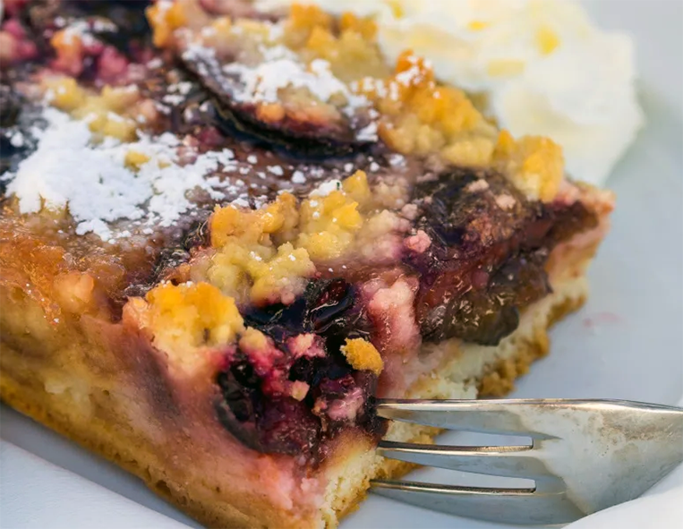 blackberry filled lightning cake with streusel topping served on a plate with sour cream