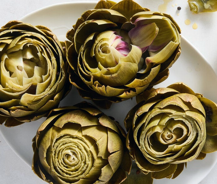 four boiled artichokes trimmed and arranged on a plate