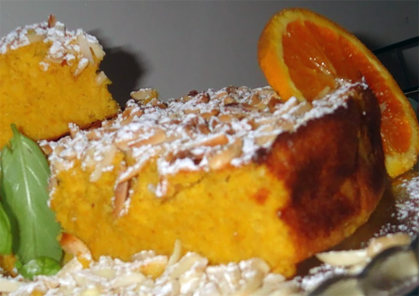 slice of Mozambican orange and almond cake topped with orange icing and served with a slice of orange