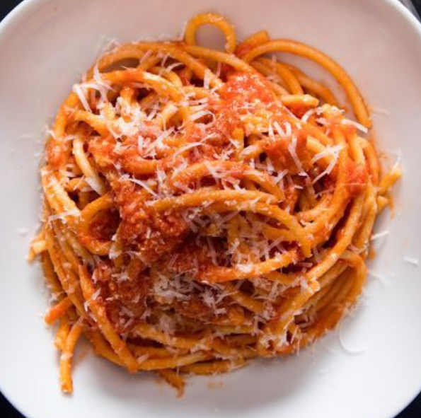 bucatini pasta tossed with amatriciana sauce of guanicale and chilli flakes in a wine and tomato base served garnished with pecorino romano on a white plate