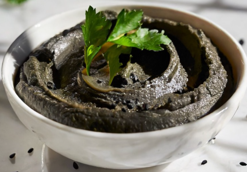 hummus of black carlin peas in a white bowl with a flat-leaf parsley garnish