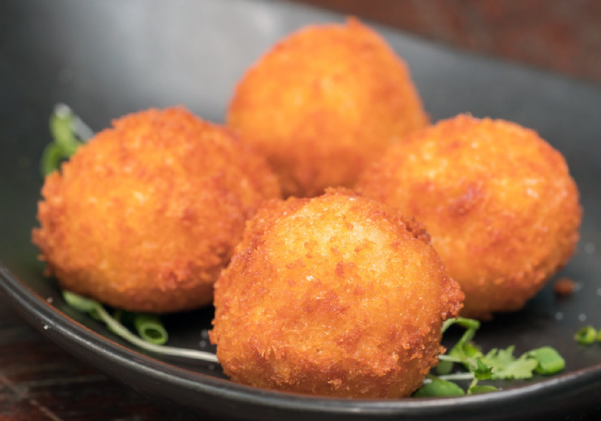 four breaded champ balls in a dish with micro greens