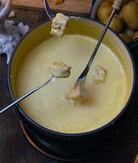 melted cheese in a pan with bread on long forks being dipped in it