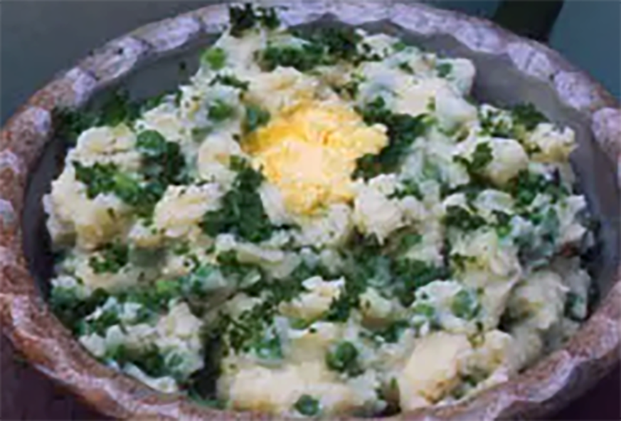 champ of mashed potatoes, kale, peas and spring onions with cheese in a wooden bowl topped with a pat of butter
