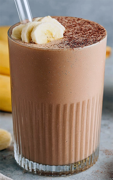chocolate banana smoothie in a glass topped with grated chocolate and banana slices