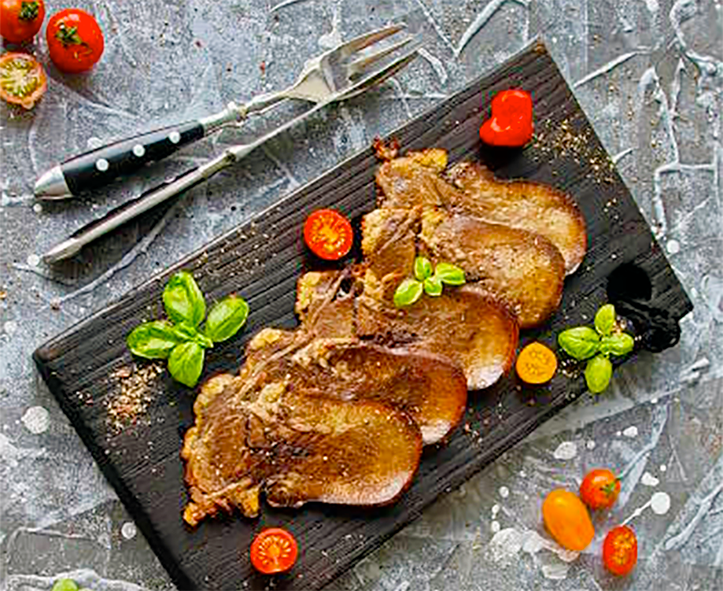 slices of cold-pressed ox tongue presented on a slate dish with halved cherry tomatoes and basil