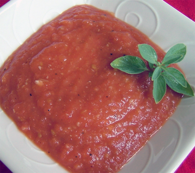 cooked tomato coulis in a square bowl with a sprig of oregano