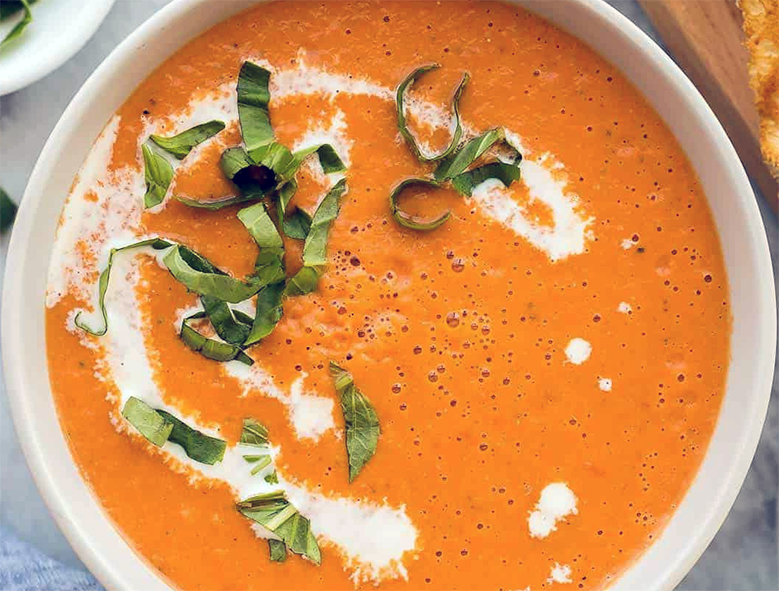 creamy tomato soup served in a bowl with a swirl of cream and a garnish of shredded basil