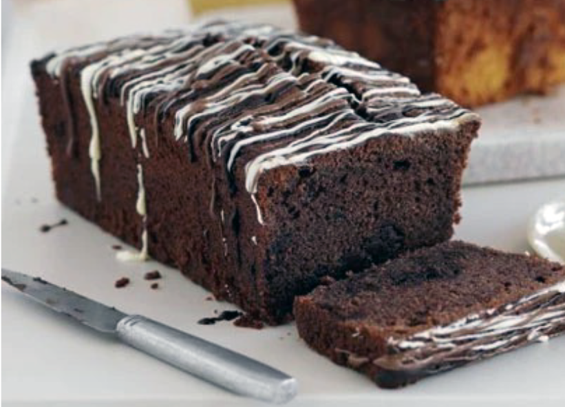 double chocolate loaf cake with white chocolate drizzle on a chopping board with one slice cut off