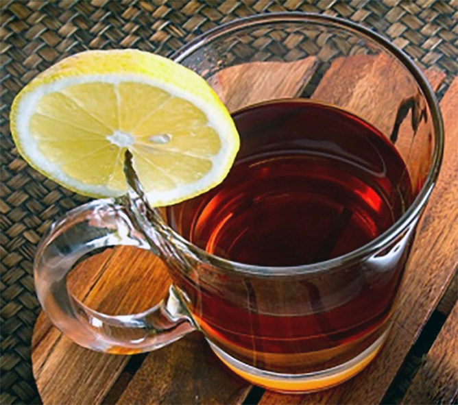 safflower petal tea served in a glass cup with a slice of lemon to garnish