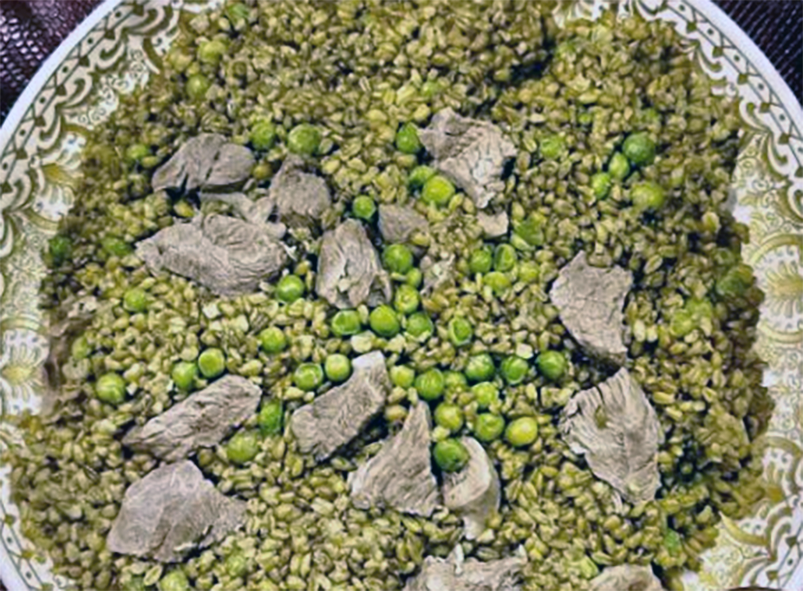 Syrian freekeh served on a plate topped with peas and rice