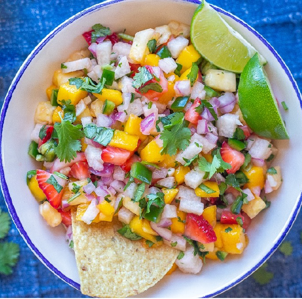 fruit salsa in a bowl with lime wedges and a tortilla chip