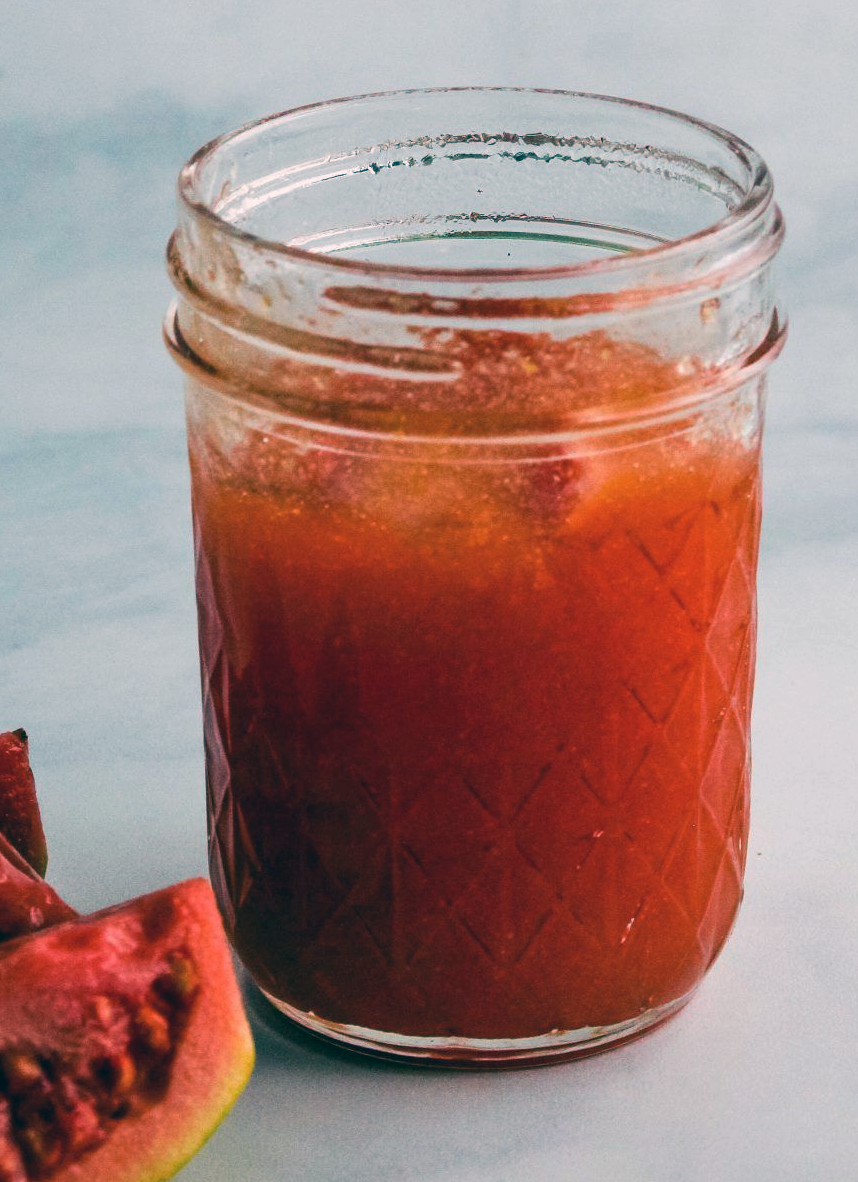 guava jelly in a glass jar next to a piece of guava