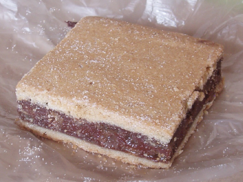 Square slice of Irish gur cake with a filling of bread, spice, dried fruit and brown sugar bound with egg between two sheets of pastry on a sheet of plastic