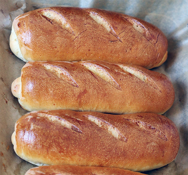 three home-made hoagie rolls on a paper lined baking tray