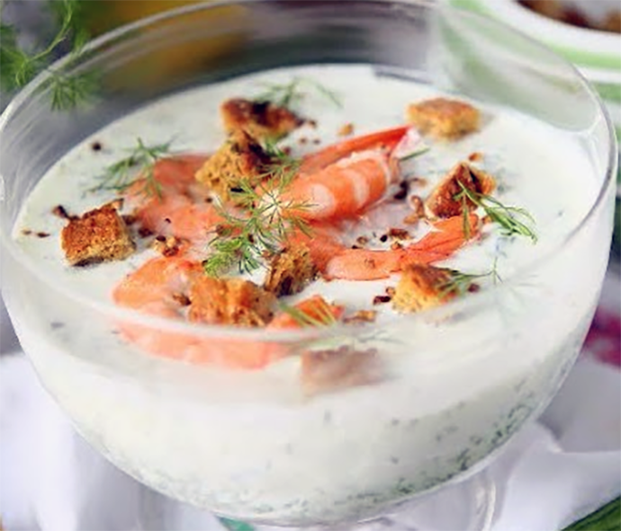 Iced yoghurt soup with cucumbers, gherkins and prawns served in a glass dish with dill garnish