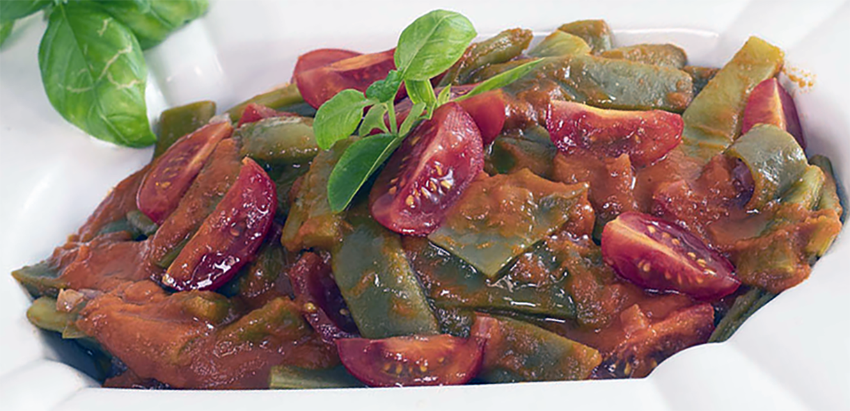 Green beans in tomato sauce served in a white dish with a garnish of basil
