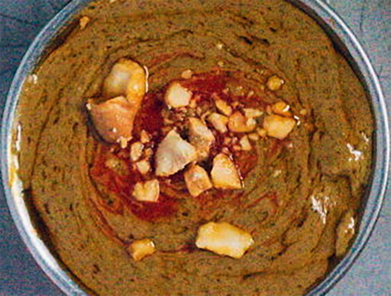 sauce of moringa leaves in a tomato and peanut base served in a bowl garnished with chopped peanuts and chilli powder