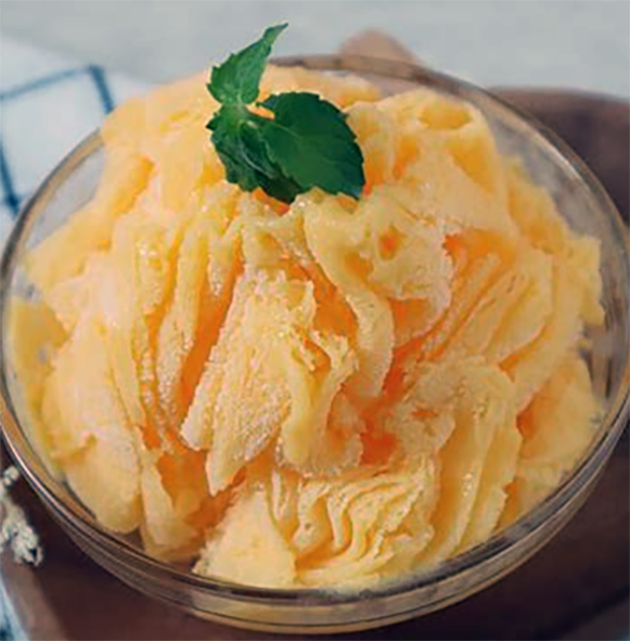 Mango snow served in a glass bowl topped with a sprig of mint