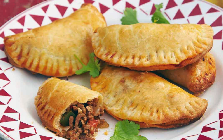 baked beef empanadas arranged on a plate with one split open to reveal the filling