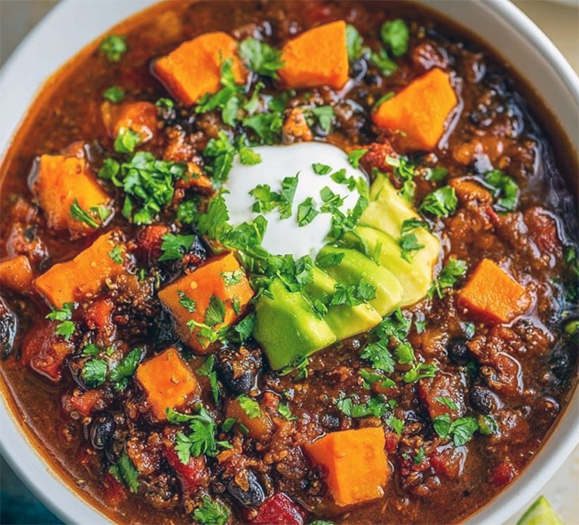 mole-style sweet potato chilli garnished with avocado, sour cream, sweet potato chunks and coriander leaves in a bowl