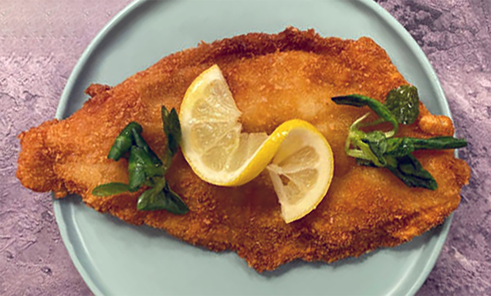 fried breaded plaice topped with a slice of lemon on a green plate
