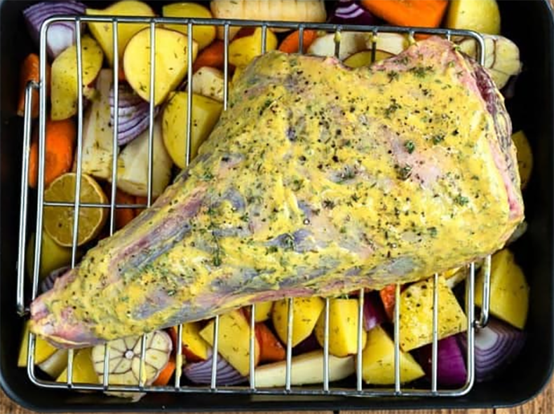 mustard-coated leg of lamb set over a bed of vegetables ready for roasting