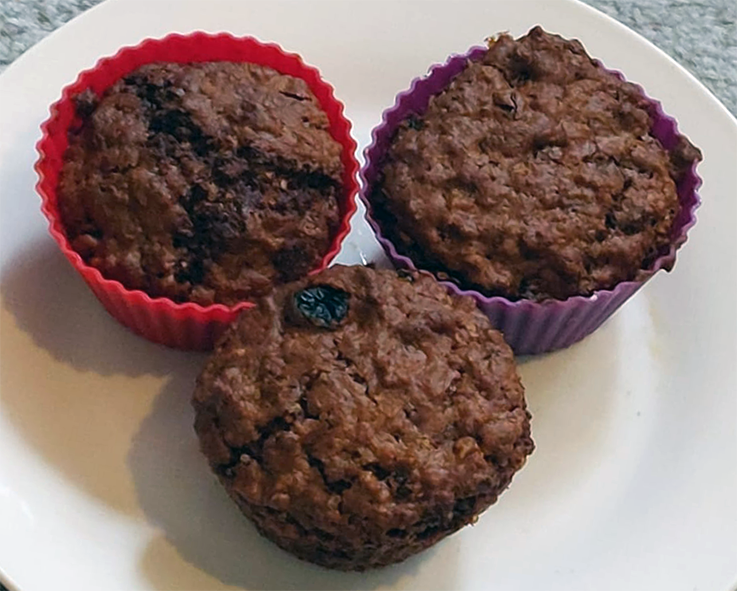 three oat and jam muffins on a plate with one taken out of its silicone baking case