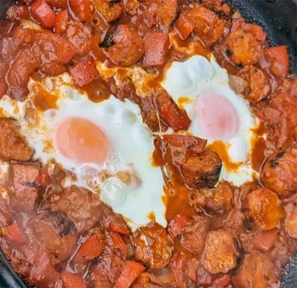 Eggs frying in a tomato and merguez sausage base in a large frying pan