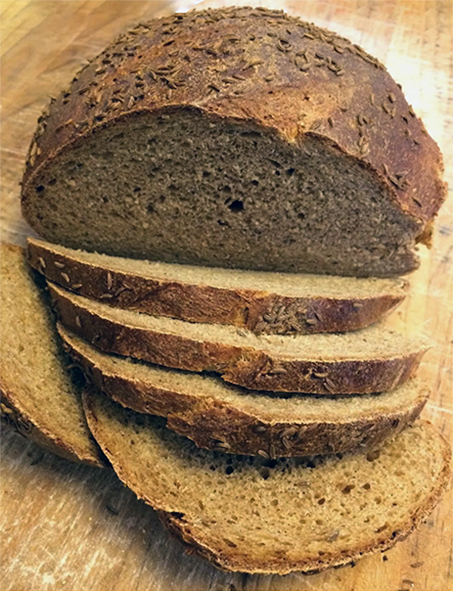 old world rye bread baked as a cob loaf, shown sliced on a chopping board