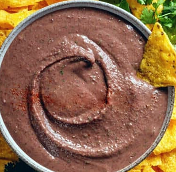 pureed black bean and onion dip with a corn chip in a bowl