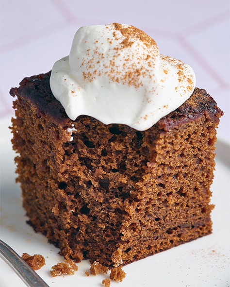 piece of Mozambican pao de miel (honey, almond and molasses cake) on a plate topped with cream and cinnamon