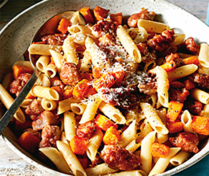 penne pasta with pumpkin and sausage in a cocotte with a spoon