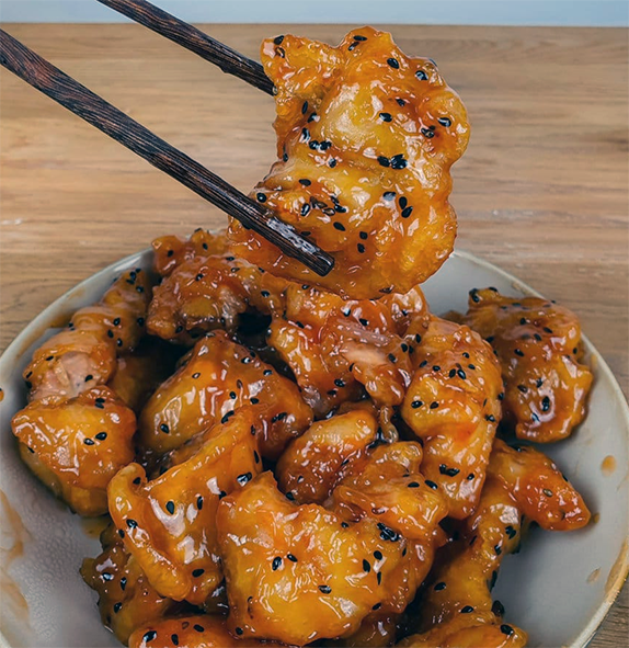 sweet and sour pork on a plate with one piece lifted with chopsticks)
